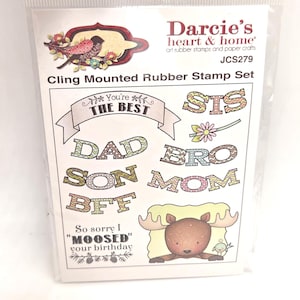 May include: A cling mounted rubber stamp set by Darcie's heart & home. The set includes stamps with the words "DAD", "SON", "BFF", "BRO", "MOM", "STS", and "You're the Best". Also included is a moose and a bird illustration. The set is packaged in a clear plastic bag.