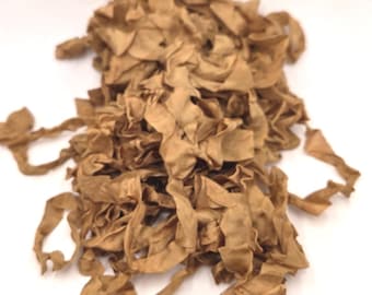 May include: A pile of tan-colored fabric ribbon with a textured, slightly wrinkled surface. The ribbon is loosely gathered in a heap, showing multiple strands and frayed edges throughout the tangled, light brown textile material.