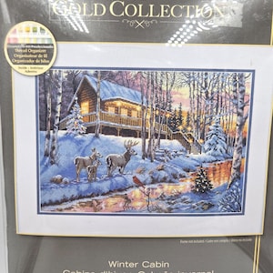 May include: A cross stitch kit titled The Gold Collection Winter Cabin featuring a snowy landscape with a wooden cabin, a group of deer, a red cardinal, and a stream. The packaging includes a thread organizer and displays the text Winter Cabin.