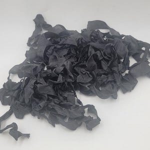 May include: A pile of black fabric ribbon, crumpled and tangled together. The ribbon is soft and silky, and it would be perfect for crafting or decorating.