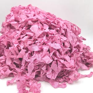 May include: A pile of pink fabric strips with a ruffled texture. The strips are bunched together, creating a dense, textured appearance. The fabric has a slightly shiny finish, and the color is a vibrant, medium pink.