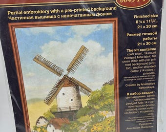 May include: A RIOLIS 0045 PT partial embroidery kit featuring a windmill landscape with a pre-printed background. The packaging displays the finished size of 8 1/4 by 11 3/4 inches and lists contents including Zweigart Aida fabric, Anchor cotton threads, and a needle.