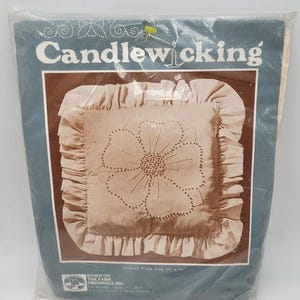 May include: A packaged Candlewicking pillow kit. The pillow has a beige floral design with a ruffled edge. The finished pillow size is 14 x 14 inches. The packaging is blue and brown with the words "Candlewicking" in white.