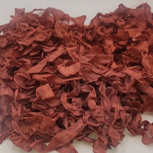 May include: A pile of rust-colored fabric ribbon scraps. The ribbon is soft and crinkled, creating a textured look.