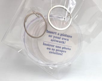 May include: Two clear circular plastic keychains with metal split rings, packaged in a transparent plastic bag. The white paper insert inside features the blue text: Insert a picture or your own artwork! Insérer une photo ou sa propre création!
