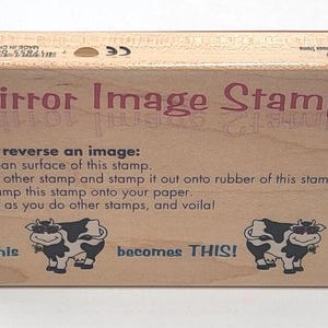 May include: Wooden mirror image stamp with instructions. The stamp has the words "Mirror Image Stamp" in a mirrored font. Below the instructions are two cartoon cows wearing sunglasses. The text "This becomes THIS!" is also present.