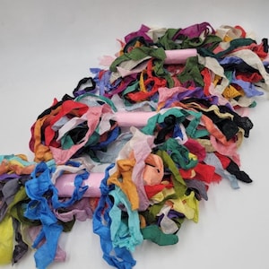 May include: Three bundles of colorful fabric scraps tied together with pink ribbon. The fabric scraps are a variety of colors and textures, including blue, green, red, yellow, and orange.