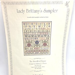 May include: A cross-stitch sampler kit titled "Lady Brittany's Sampler." The design includes an alphabet, numbers, and decorative floral and geometric patterns. The kit is designed by Darlene G. O'Steen and worked on linen.