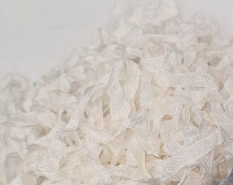 May include: A close-up view of a pile of white, textured ribbons. The ribbons are loosely arranged, creating a layered effect. The ribbons appear to be made of a delicate, possibly sheer material, with a subtle sheen. The background is a soft, off-white color.
