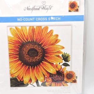May include: A Needleart World no-count cross stitch kit featuring a large yellow and orange sunflower design. The packaging includes the text Sunflower, 640.085, and Precise Color Print on Aida. The kit displays a finished sunflower image.