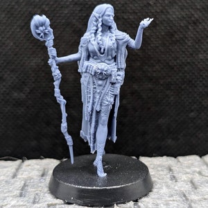 May include: A detailed, light blue figurine of a female fantasy character. She is depicted with long hair, intricate clothing, and a staff topped with a flower. The figure is standing on a black circular base, with one arm outstretched.