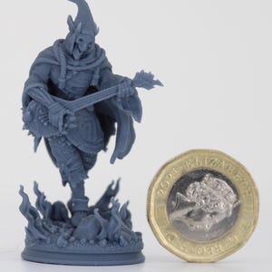 May include: A grey miniature figurine of a skeletal figure playing a guitar. The figure wears a hooded cloak and stands on a base with flame details. A one-pound coin is next to the figurine for scale.