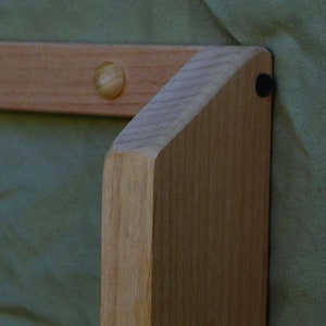 May include: Close-up of a wooden frame with a rounded corner and a small wooden knob. The frame is made of light-colored wood and has a natural finish.