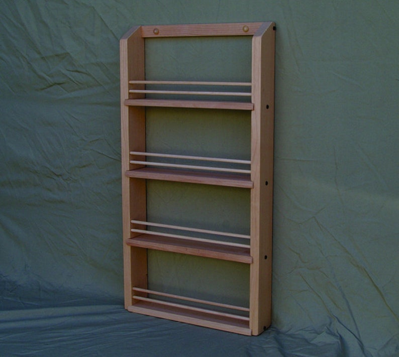May include: A wooden spice rack with four shelves and a light wood finish. The rack is mounted on a wall and has a green background.