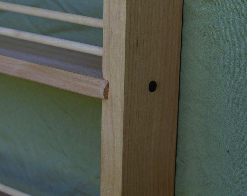 May include: Close-up of a wooden shelf unit with a light wood finish. The shelf is attached to a wall and has a small black dot on the side.