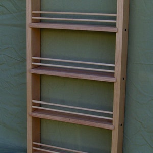 May include: A wooden spice rack with four shelves and a bottom shelf. The rack is made of light wood and has a natural finish. It is mounted on a wall.