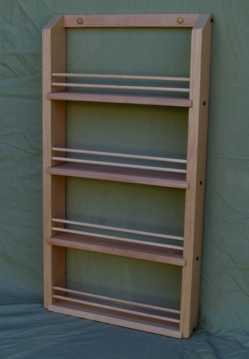 May include: A wooden spice rack with four shelves and a bottom shelf. The rack is made of light wood and has a natural finish. It is mounted on a wall.