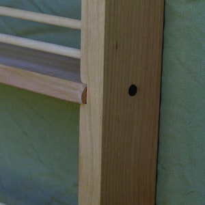 May include: Close-up of a wooden shelf unit with a light wood finish. The shelf is attached to a wall and has a small black dot on the side.