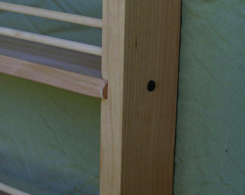 May include: Close-up of a wooden shelf unit with a light wood finish. The shelf is attached to a wall and has a small black dot on the side.