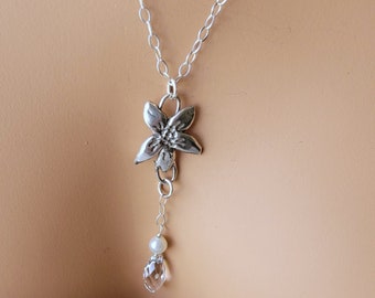May include: A silver chain necklace with a flower pendant and a crystal bead. The flower pendant has a textured surface and the crystal bead is clear.