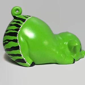 May include: Green ceramic piggy bank with black and white stripes and white dots. The piggy bank is lying on its side with its head resting on the ground.