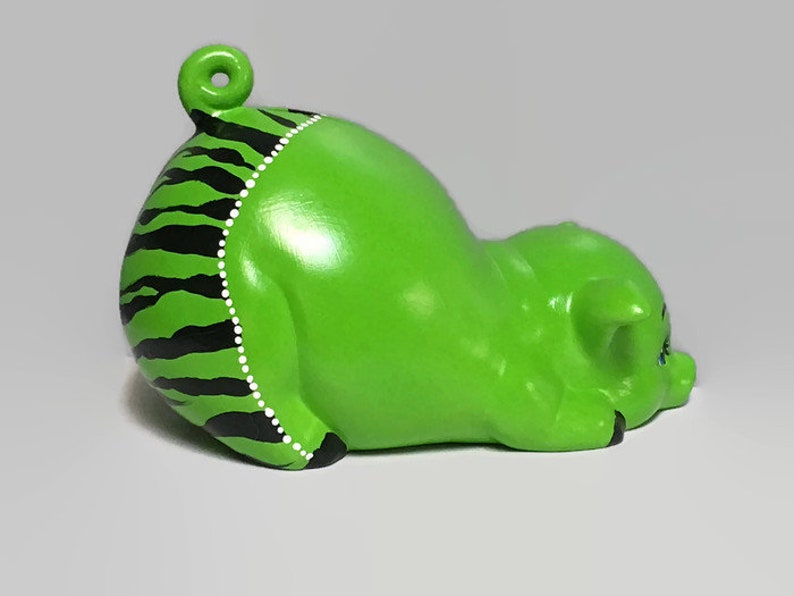 May include: Green ceramic piggy bank with black and white stripes and white dots. The piggy bank is lying on its side with its head resting on the ground.