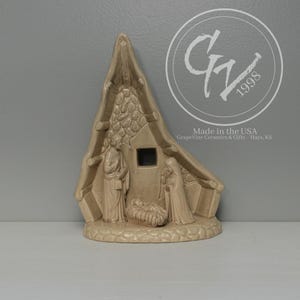 May include: A beige ceramic nativity scene depicting the holy family inside a stable. The scene includes figures of Mary, Joseph, and baby Jesus in a manger. The structure has a stone-like texture and is made in the USA.