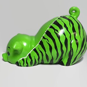 May include: Green ceramic piggy bank with black and white stripes painted on the body. The piggy bank is lying on its side with its head turned to the left.