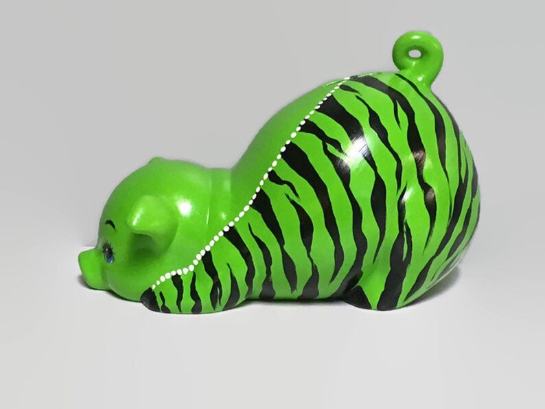 May include: Green ceramic piggy bank with black and white stripes painted on the body. The piggy bank is lying on its side with its head turned to the left.