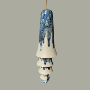 May include: A white ceramic wind chime with four tiers. The top tier is decorated with blue and green glaze, while the lower tiers have a white glaze with blue and green accents.