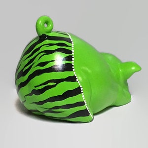 May include: Green ceramic piggy bank with black and white zebra stripes painted on the back. The piggy bank has a small tail and a curled tail.