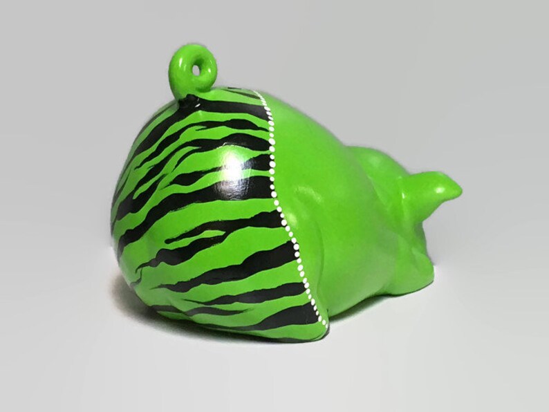 May include: Green ceramic piggy bank with black and white zebra stripes painted on the back. The piggy bank has a small tail and a curled tail.