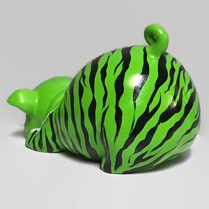 May include: A green ceramic piggy bank with black stripes, resembling a zebra pattern. The piggy bank is lying on its side with its tail curled up.