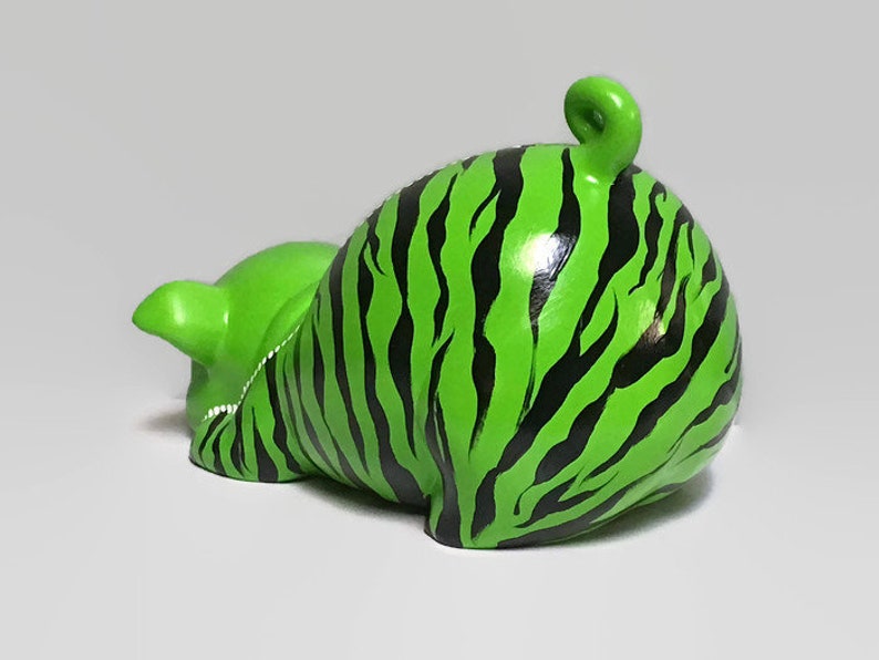 May include: A green ceramic piggy bank with black stripes, resembling a zebra pattern. The piggy bank is lying on its side with its tail curled up.