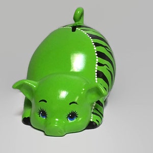 May include: Green piggy bank with black and white stripes and a white pearl design. The piggy bank has a slot on the back for coins and has blue eyes.