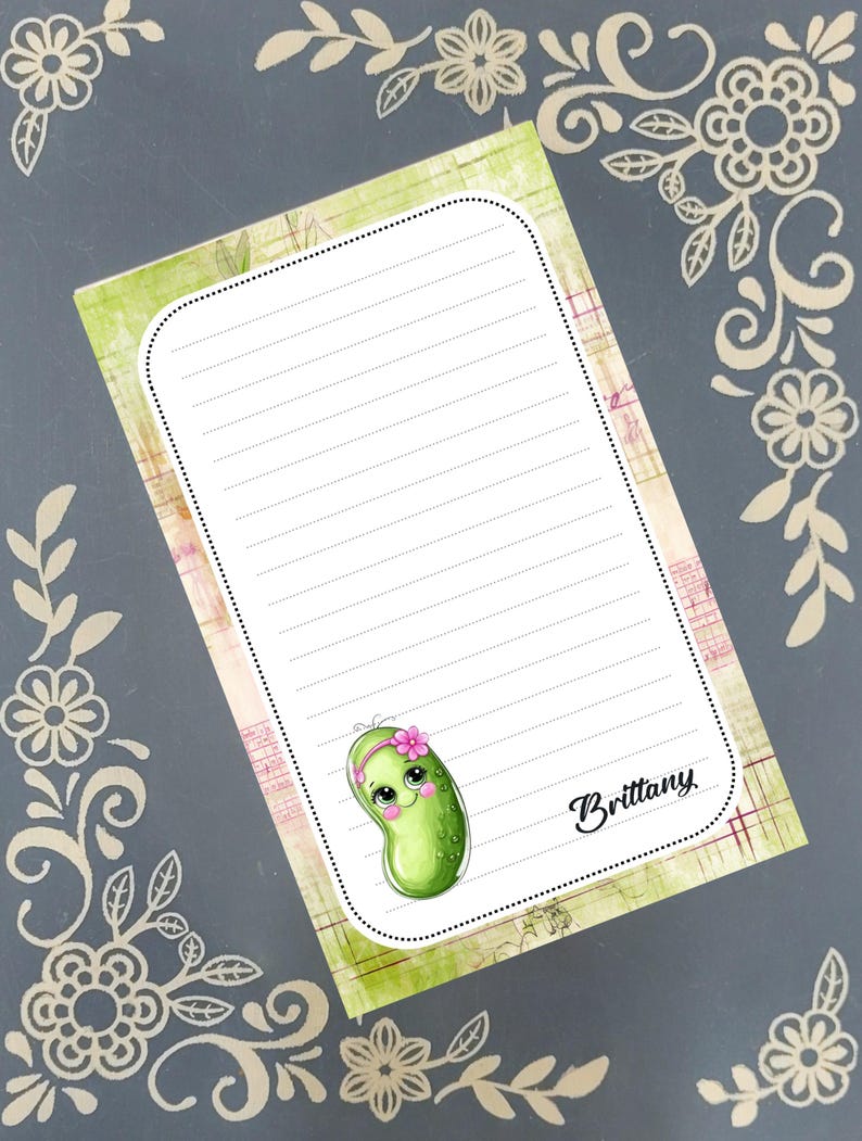 May include: A lined notepad featuring a cartoon pickle character with a pink flower headband. The notepad has a green and pink border, with the name "Brittany" in cursive. Floral decorative elements frame the notepad.