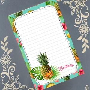 May include: A lined notepad with a tropical design. The notepad has a teal background with illustrations of pineapples, hibiscus flowers, and monstera leaves. The name "Brittany" is written in pink script on the bottom right corner.