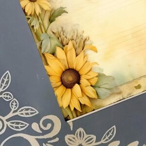 May include: Close-up of a gray frame with sunflowers and floral designs. The frame features a vintage-style background with musical notes.  The sunflowers are yellow with brown centers, and the floral accents are painted in a light beige. The frame's design incorporates both painted and stenciled elements. The overall aesthetic is rustic and charming, suitable for home decor or scrapbooking.