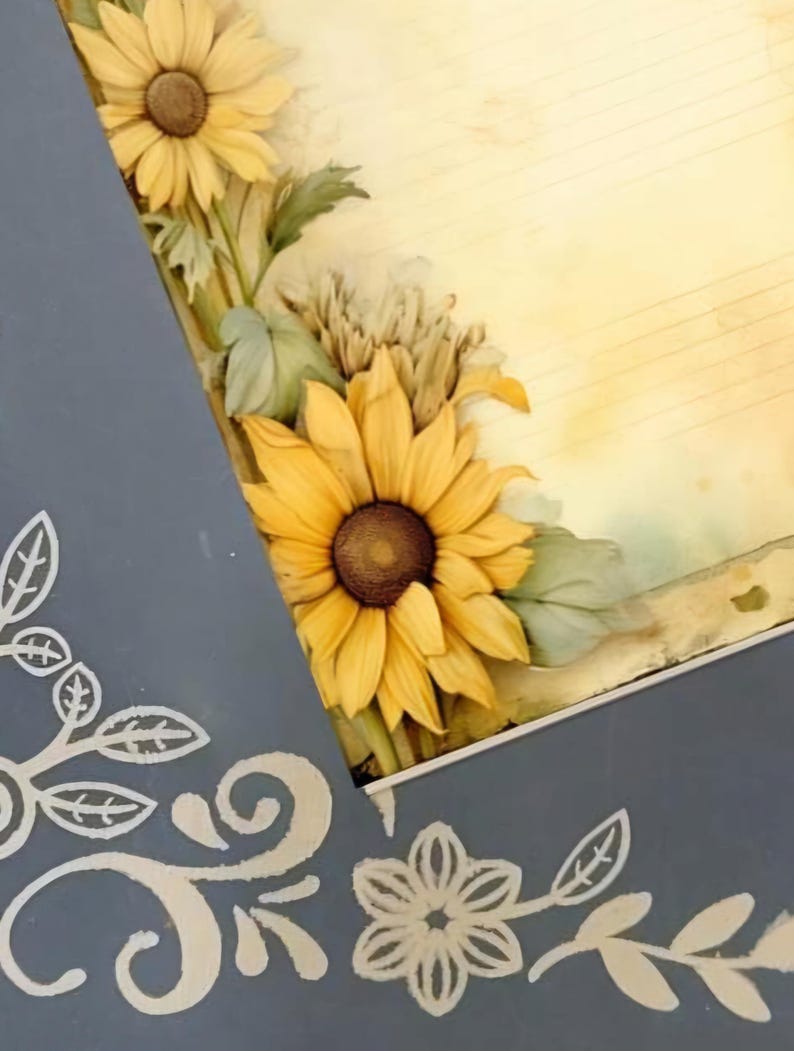 May include: Close-up of a gray frame with sunflowers and floral designs. The frame features a vintage-style background with musical notes.  The sunflowers are yellow with brown centers, and the floral accents are painted in a light beige. The frame's design incorporates both painted and stenciled elements. The overall aesthetic is rustic and charming, suitable for home decor or scrapbooking.