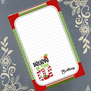 May include: A lined notepad with a red and green border, featuring the text "Believe in Your Elf." The design includes an elf hat and candy cane-striped letters. The notepad has a white background with dotted green trim.
