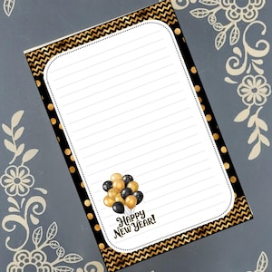 May include: A lined notepad with a black and gold chevron and polka dot border. The notepad features a cluster of gold and black balloons and the text "Happy New Year!" in a script font. The background is a muted grey with floral corner designs.