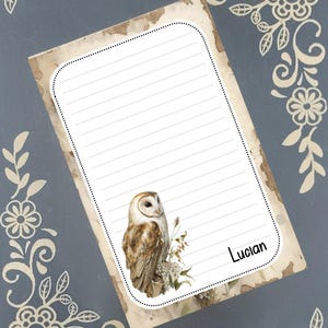 May include: A lined notepad with a vintage aesthetic, featuring a detailed illustration of a barn owl perched on a branch. The notepad has a dotted border and the name "Lucian" is written in the bottom right corner. Decorative floral elements frame the notepad.