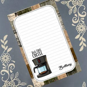 May include: Lined notepad with a coffee maker graphic and the text "But first coffee." The notepad has a decorative border and the name "Brittany" at the bottom. The background has a floral design.
