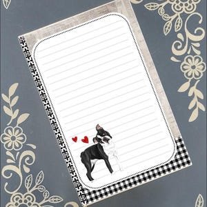 Puede incluir: Bloc de notas rayado con una ilustración de Boston Terrier y dos corazones rojos. El bloc de notas tiene un patrón de cuadros blanco y negro en la parte inferior y un borde decorativo. El fondo es un azul-gris apagado con detalles florales.