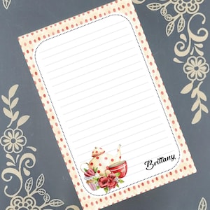 May include: A lined notepad with a dotted border and a teapot illustration. The notepad features a red and white polka dot design and the name "Brittany" in cursive. Floral corner accents frame the notepad.