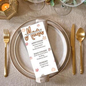 Op de afbeelding: Een Thanksgiving-menu met een witte achtergrond en bruine en oranje herfstbladeren en pompoenen. Het menu bevat voorgerechten, hoofdgerechten en desserts. De tekst luidt: "Menu Thanksgiving Voorgerechten Garnalencocktail Caesar Salad Gevulde champignons Hoofdgerecht Kruiden-gebraden kalkoen Vulling Cranberry-saus Dessert Pompoentaart Appeltaart"
