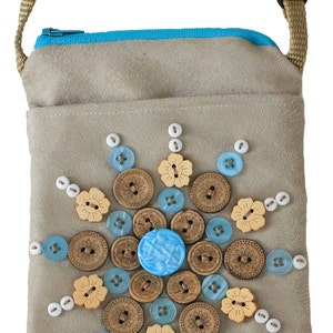 May include: A beige suede crossbody bag with a blue zipper and a decorative button design. The design features a large blue button in the center surrounded by smaller wooden buttons and white pearl-like buttons.