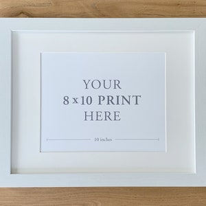 May include: White picture frame with a white mat, ready to display an 8x10 inch print. The frame has a simple, modern design and is perfect for showcasing your favorite photos or artwork.