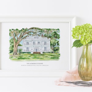 May include: A watercolor painting of a white house with a large tree in front of it. The house has a porch and a balcony. The painting is framed in a white frame and has the text "The Admiral's House, North Charleston, South Carolina" at the bottom.
