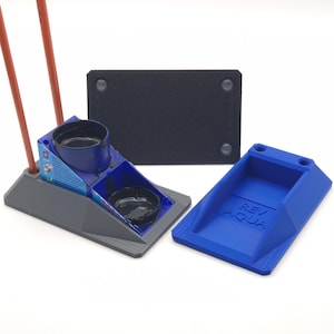 May include: A grey and blue paint holder with two red paintbrushes, a black paint tray, and a blue tray with the text "Rev/Aqua".